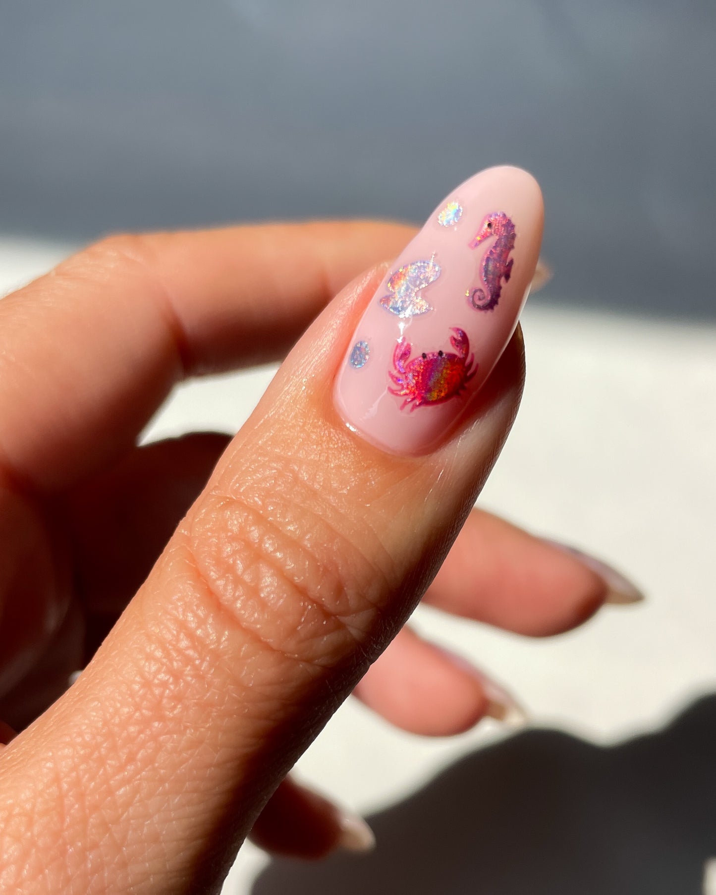 Thumb with nude pink polish and nail art stickers on