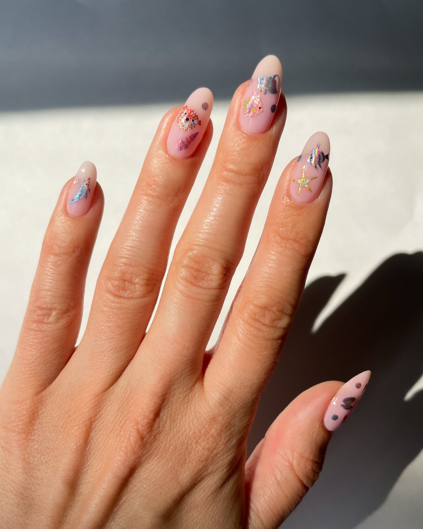 Hand with nude pink polish and nail art stickers on