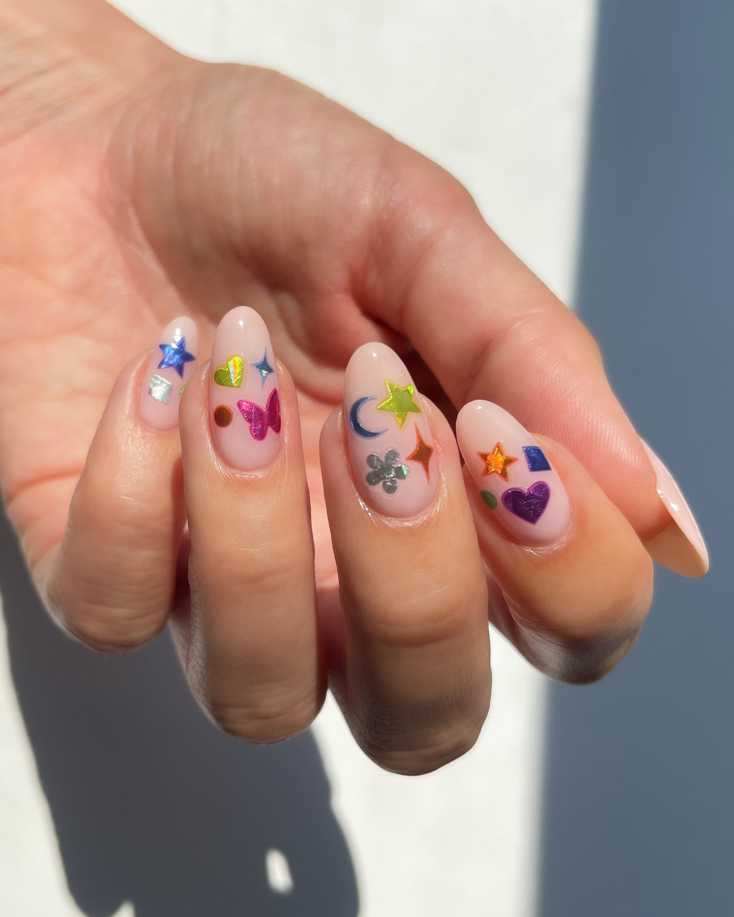 Hand with nude pink nail polish and colorful nail art stickers