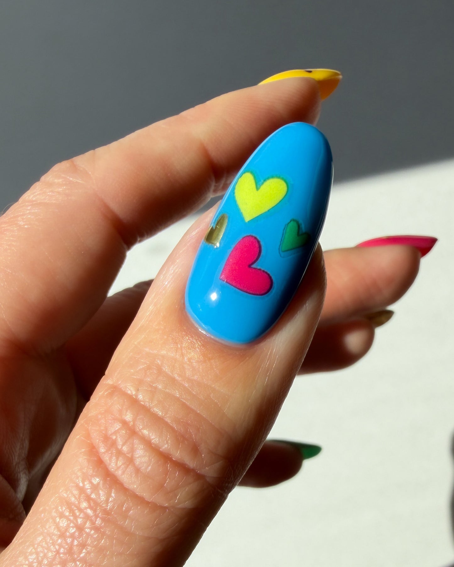 Nail with blue polish and colorful heart stickers on a neutral background
