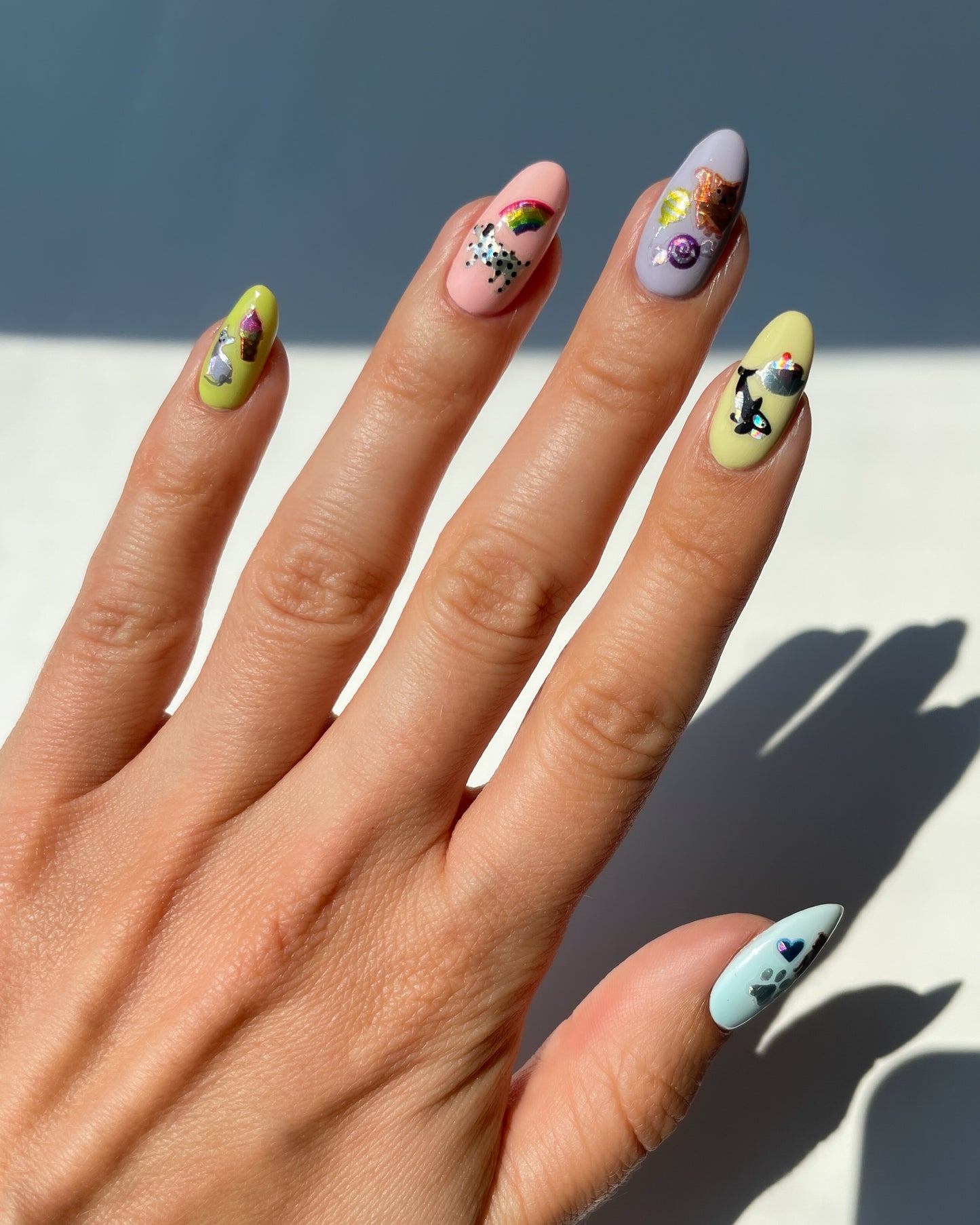 Hand with pink, blue, and yellow nails with nail art stickers on