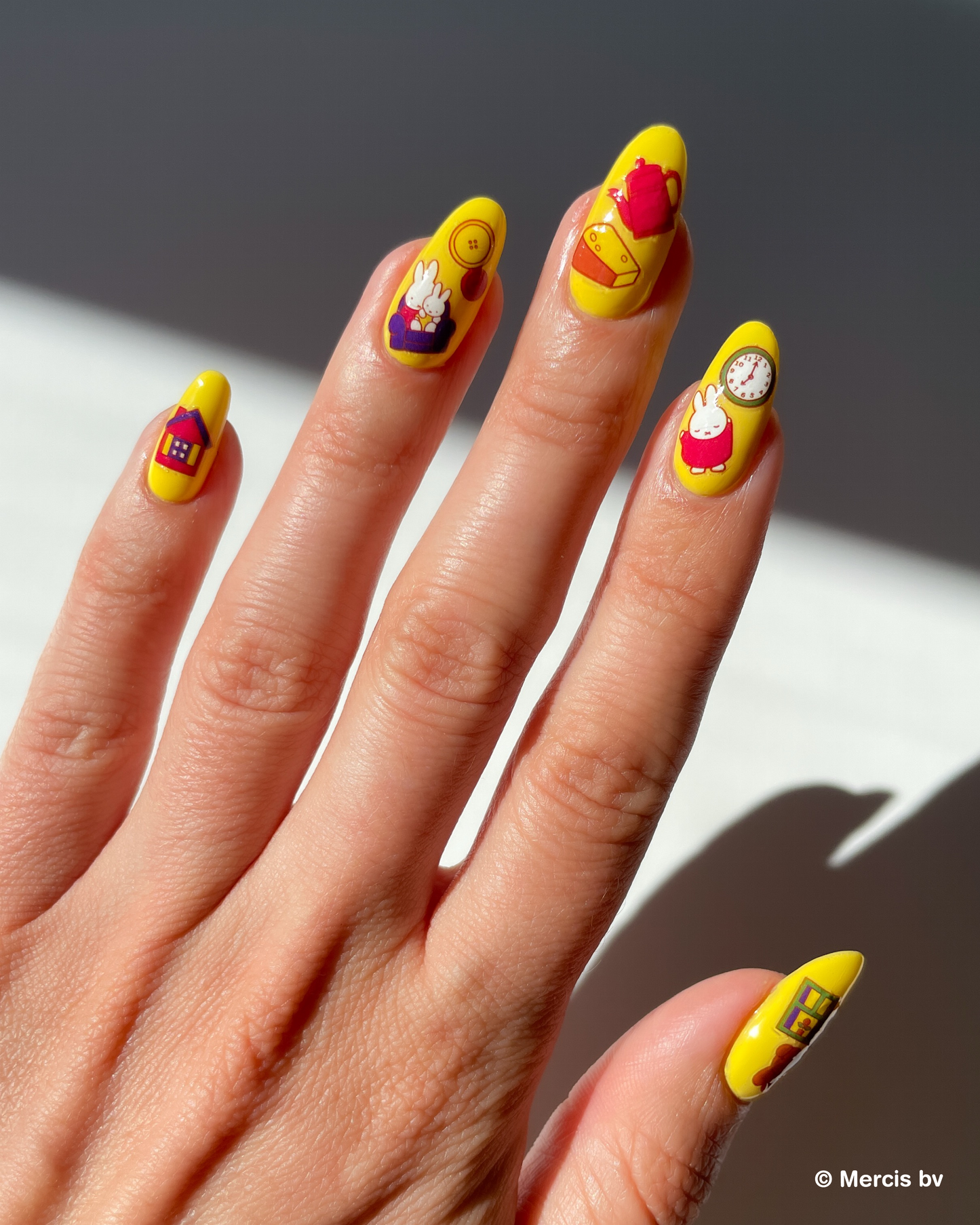 Hand with yellow nail polish and miffy nail art stickers on a neutral background
