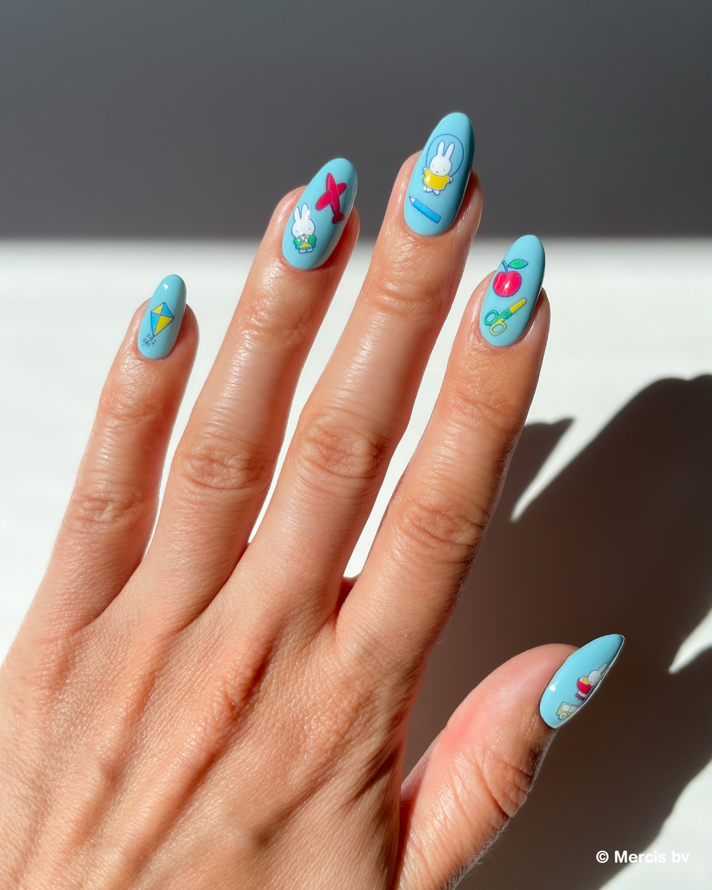 Hand with blue nail polish and miffy nail art stickers on a neutral background