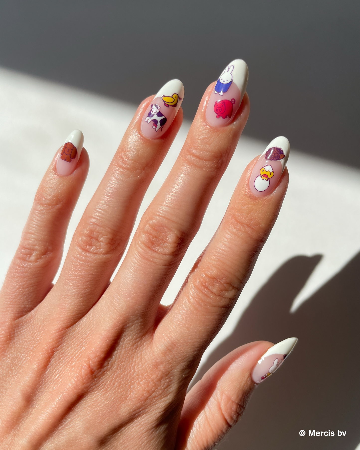 Hand with french tips and miffy nail art stickers on a neutral background