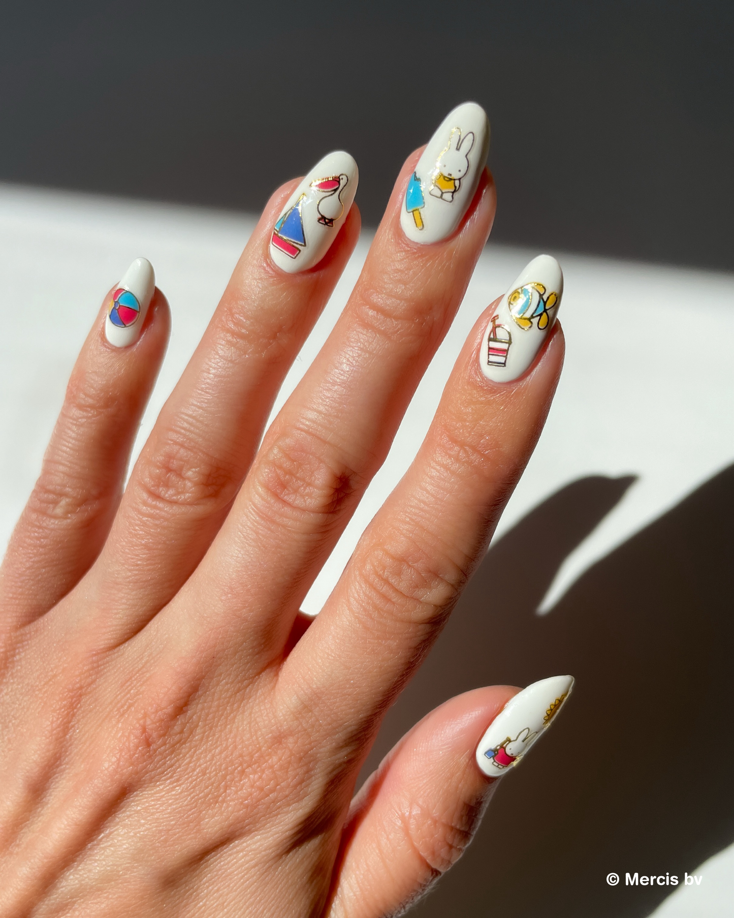 Hand with white nail polish and miffy nail art stickers on a neutral background