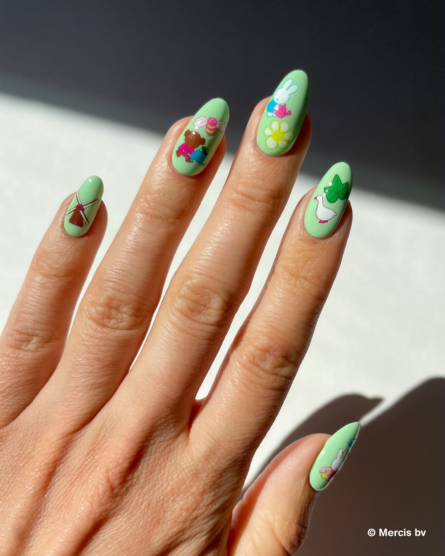 Hand with light green nail polish and miffy nail art stickers on a neutral background