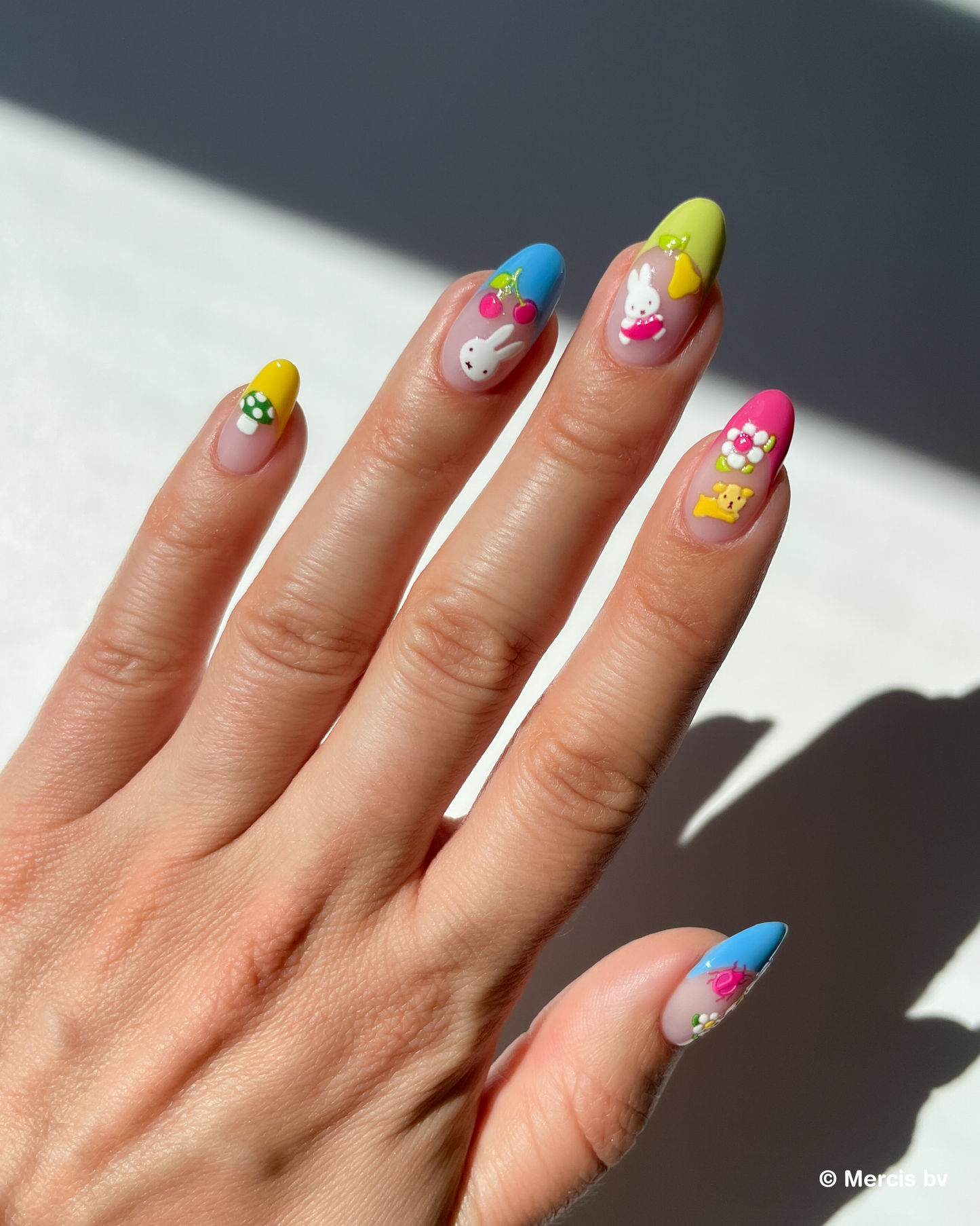 Hand with colorful french tips and puffy miffy nail art stickers on a neutral background