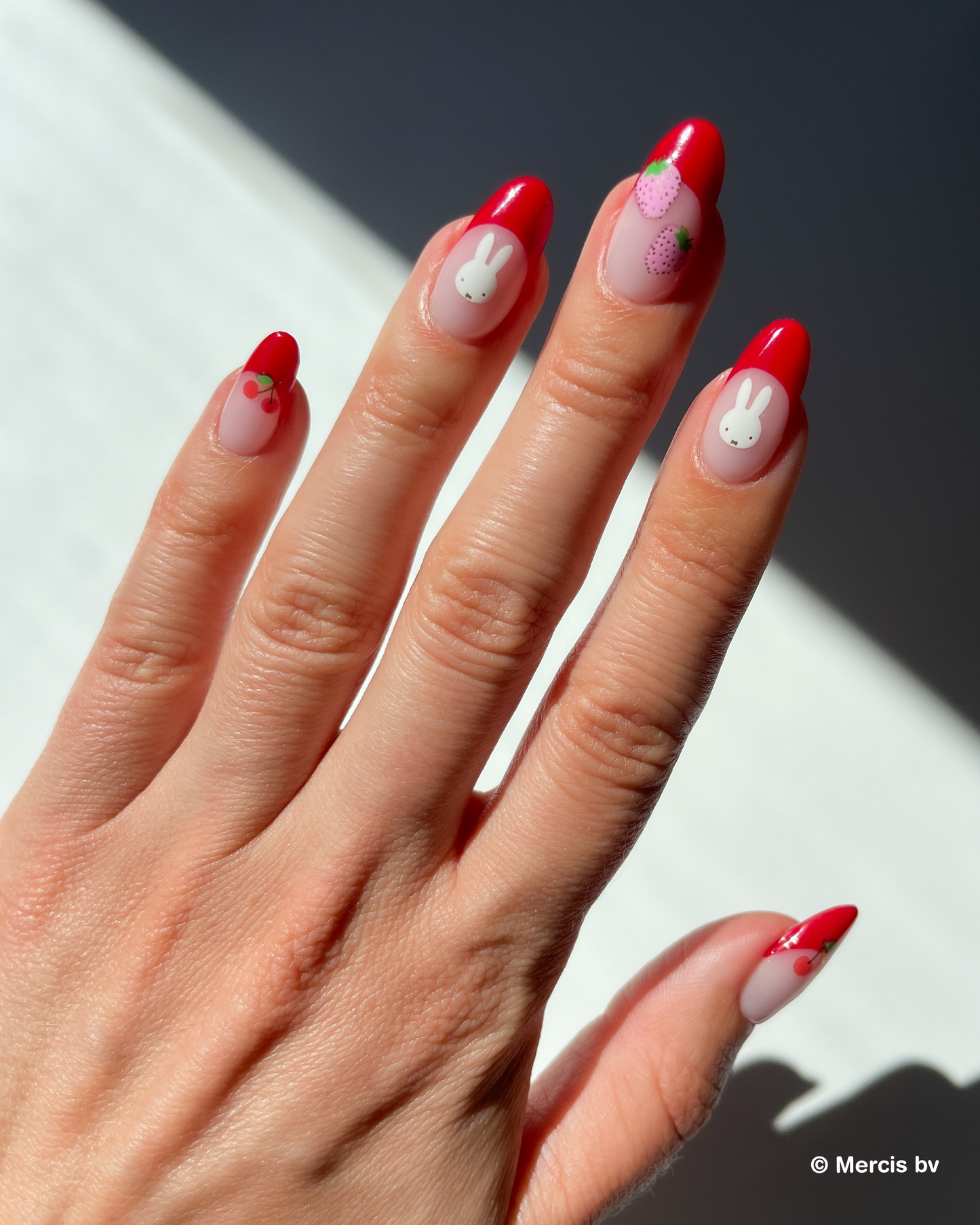 Hand with red french tips and miffy nail art stickers on a neutral background