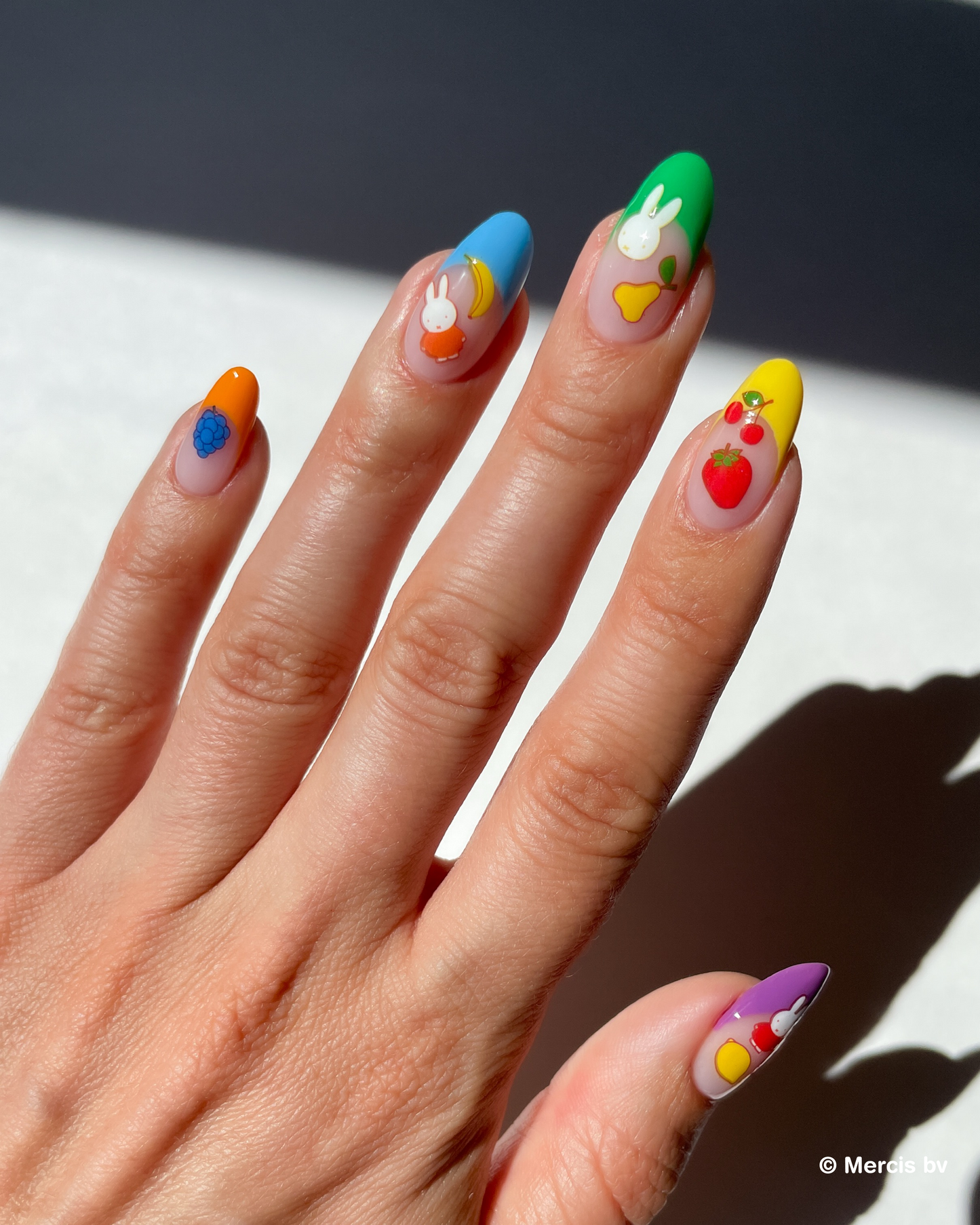 Hand with colorful french tips and miffy nail art stickers on a neutral background