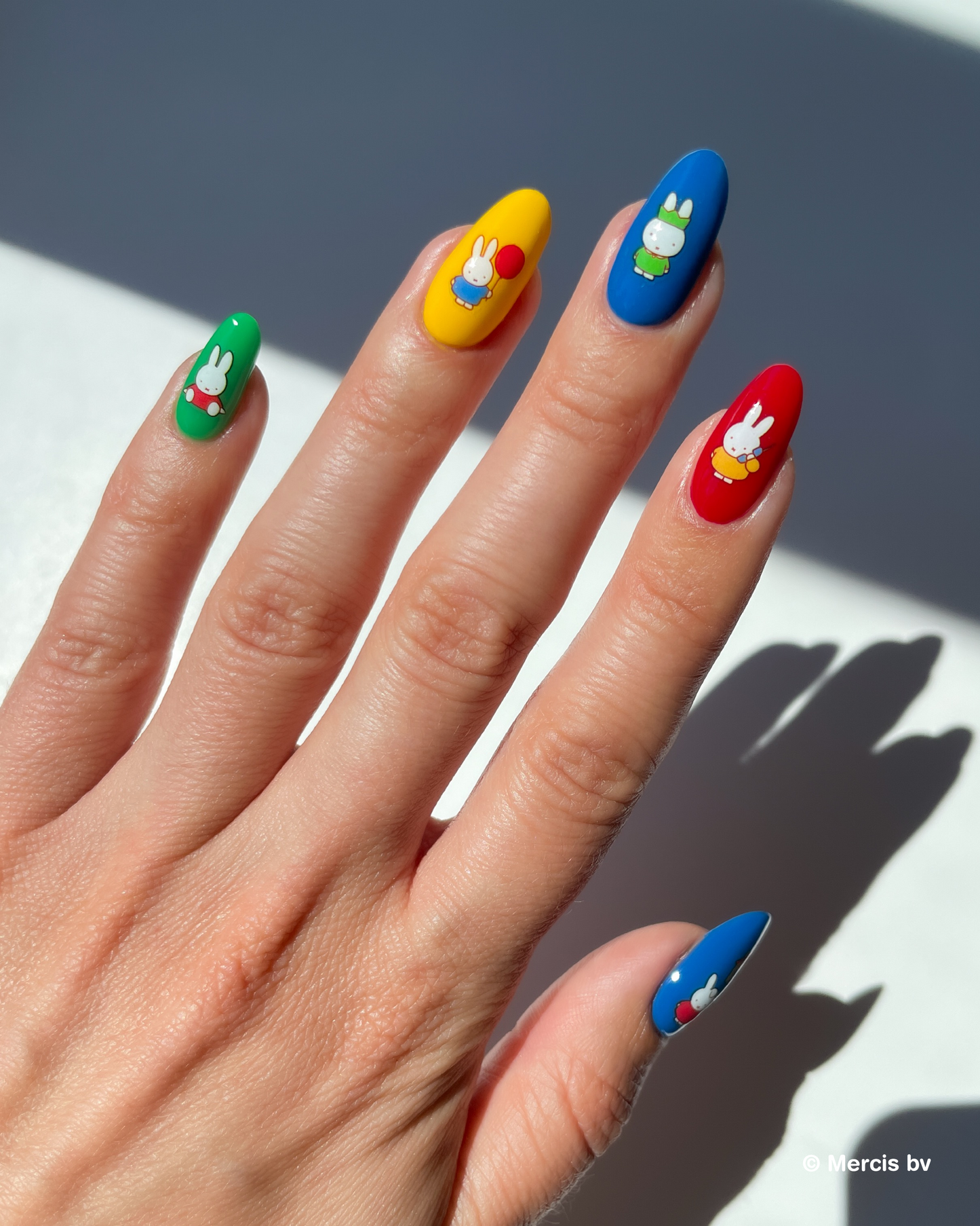 Hand with colorful nail polish and miffy nail art stickers on a neutral background
