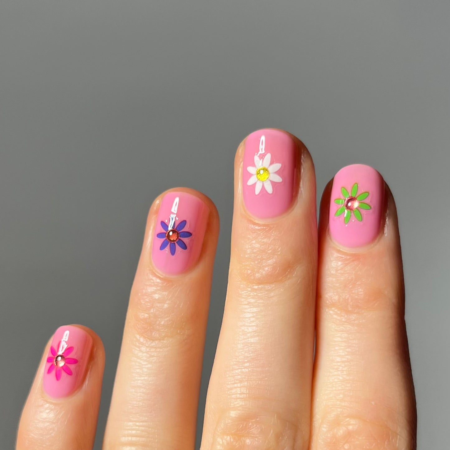 Short pink nails with flower stickers in the center