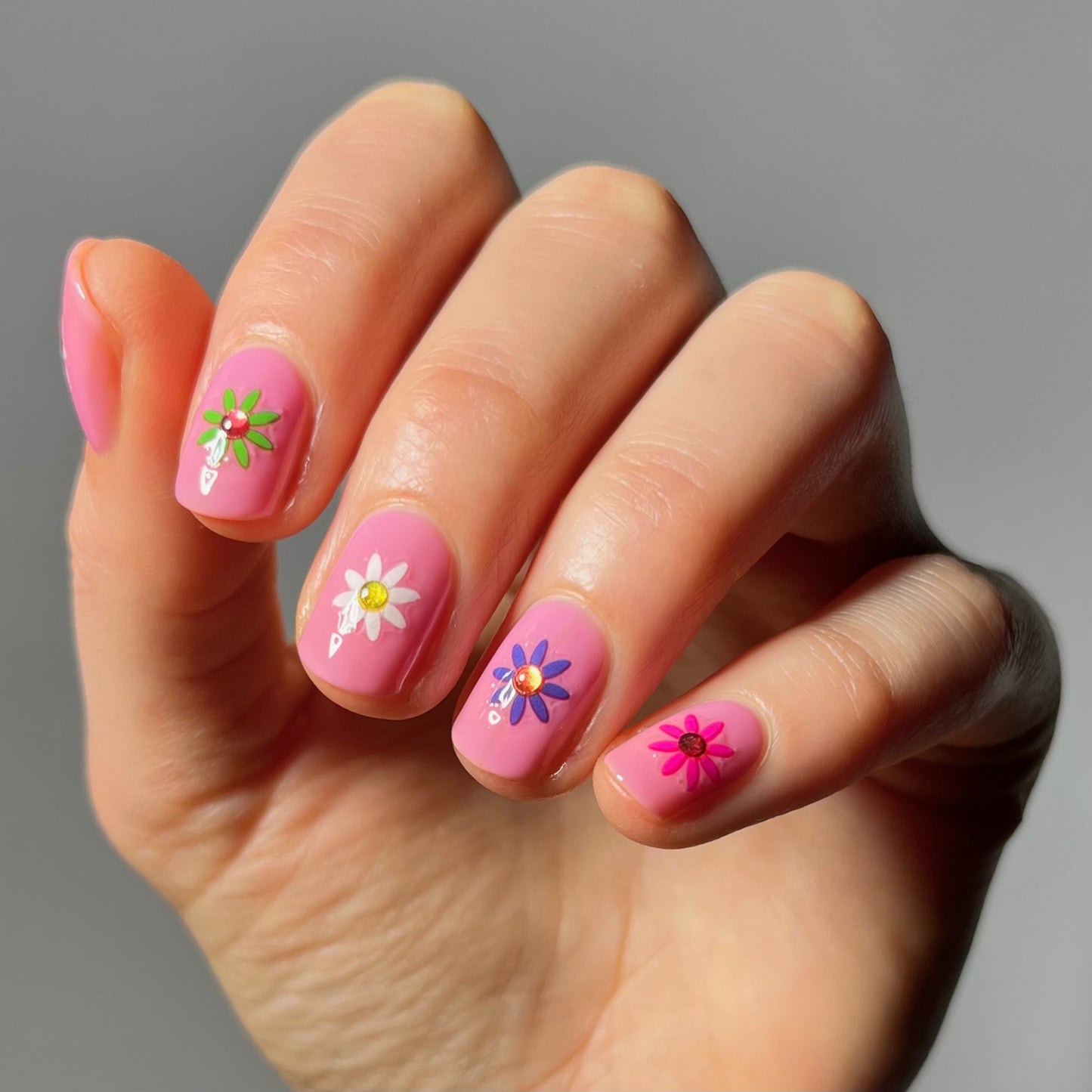 Short pink nails with flower stickers in the center