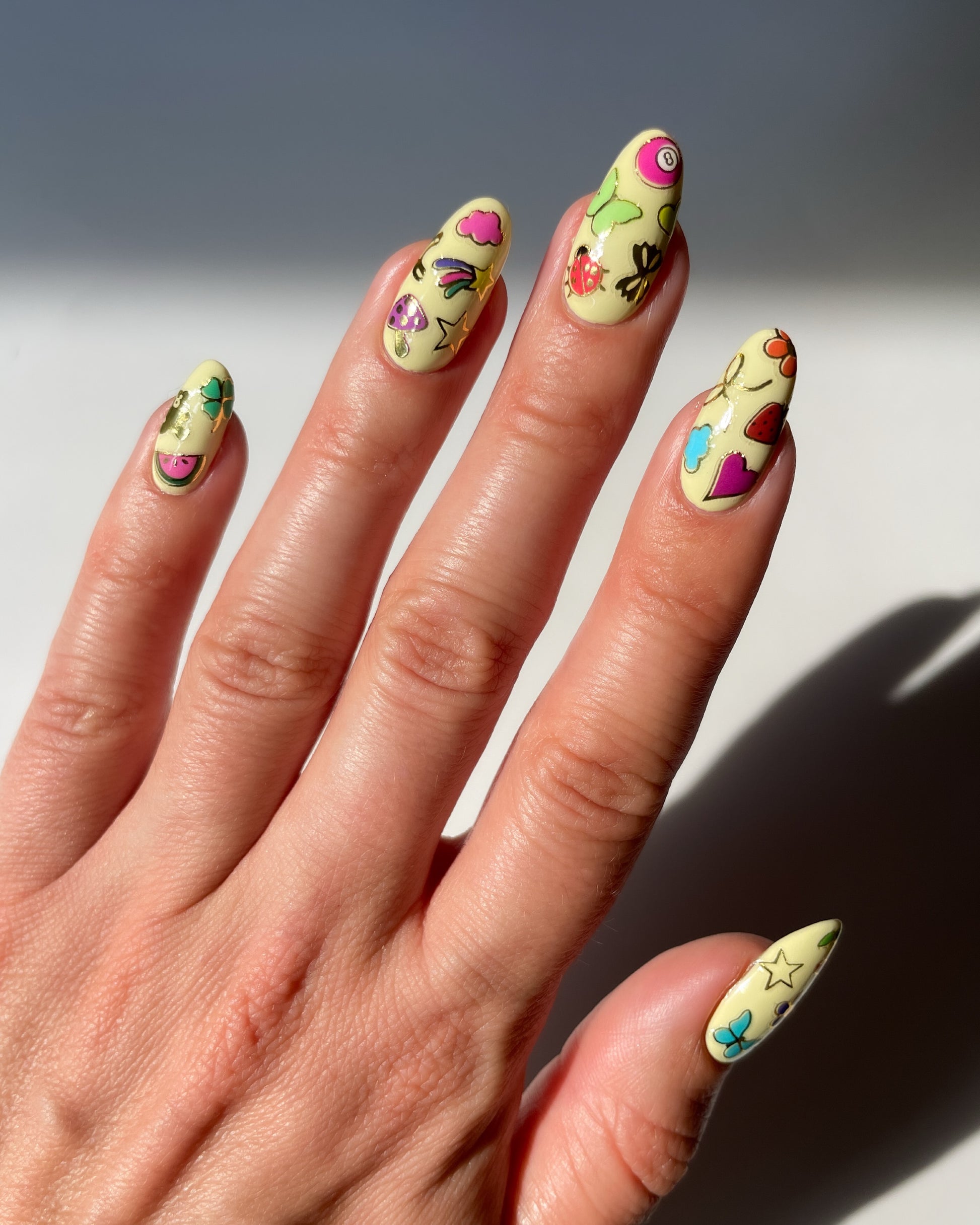 Hand with light yellow nail polish and colorful stickers on