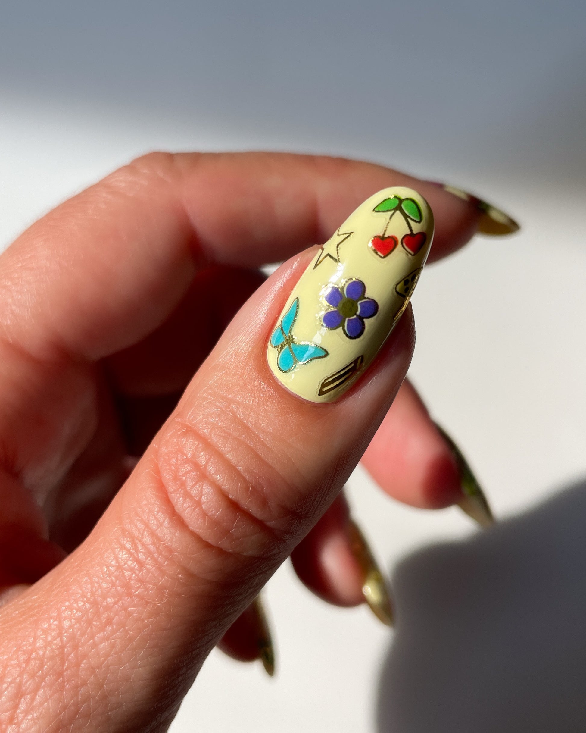 Thumb with light yellow polish and colorful stickers on