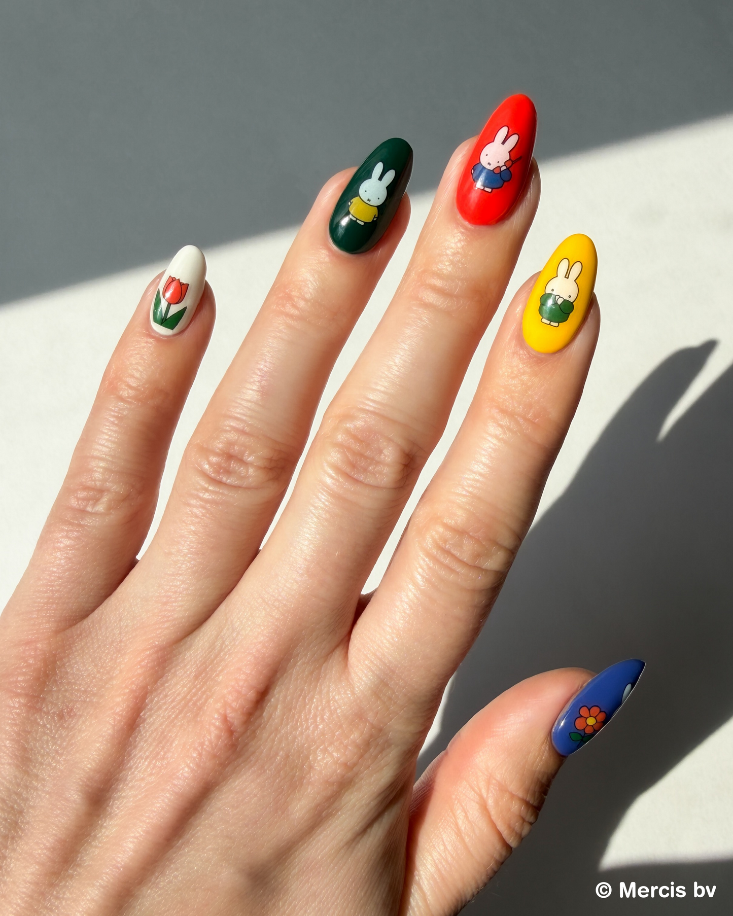 Hand with colorful nail art with Miffy stickers on a neutral background