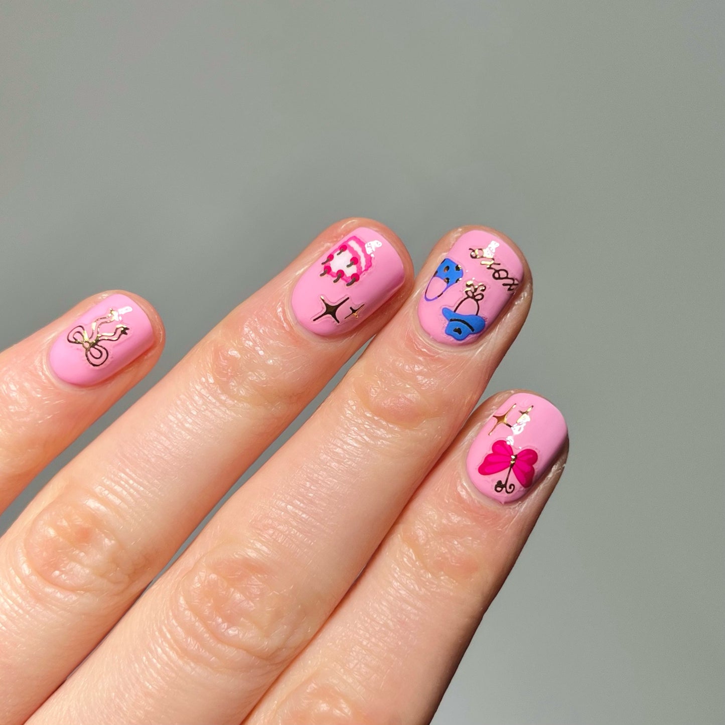 Hand with pink nail polish with nail art stickers on a neutral background