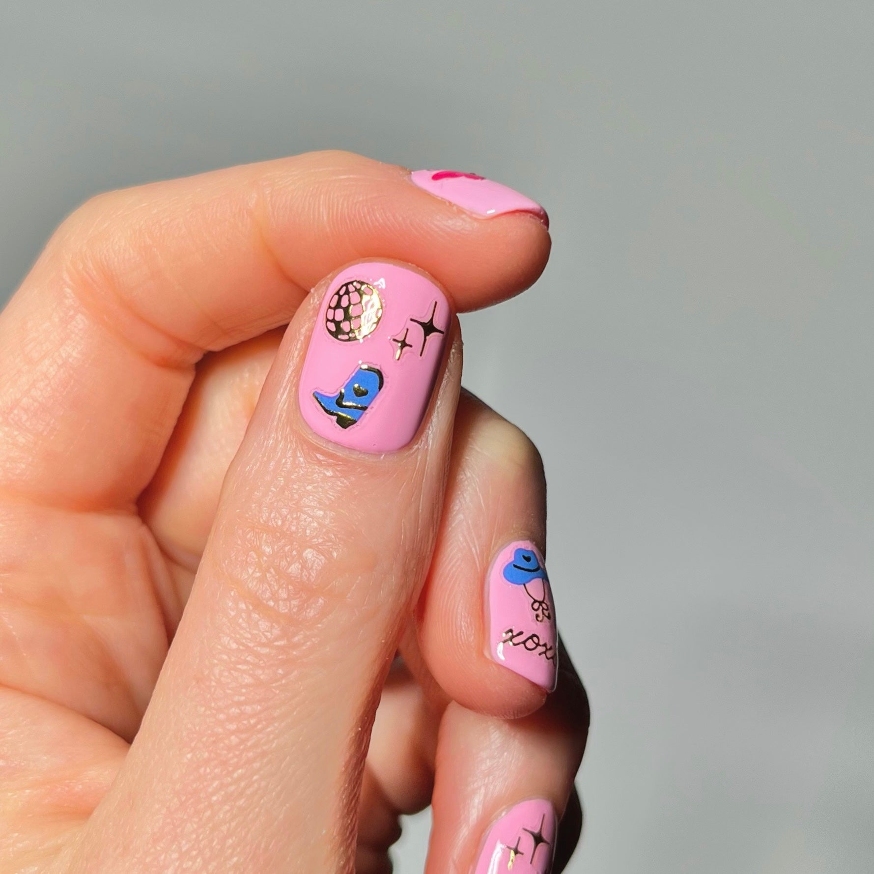 Hand with pink nail polish with nail art stickers on a neutral background