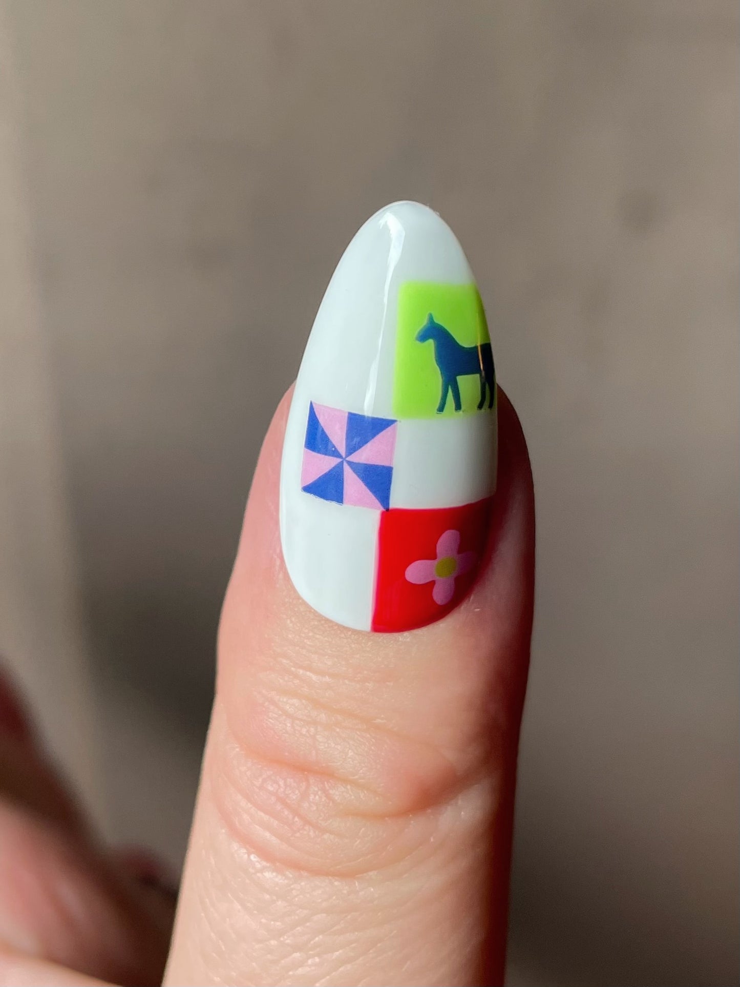 Close up of a thumb nail with a white base and stickers from the Pinwheel nail art sheet