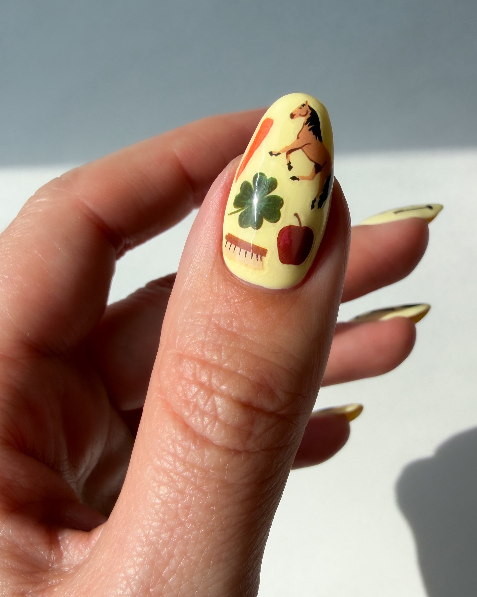 Thumb with yellow nail polish and Horse girl nail art stickers