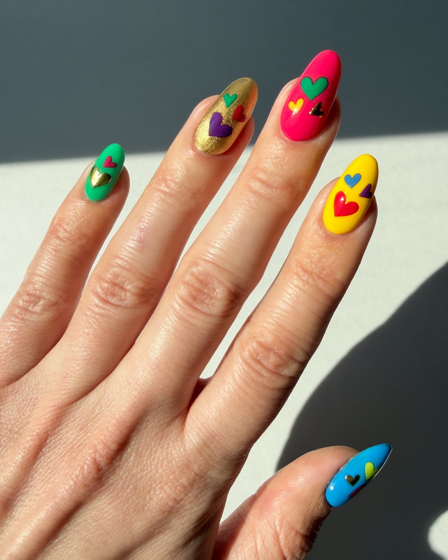 Hand with colorful nails and heart stickers on a neutral background