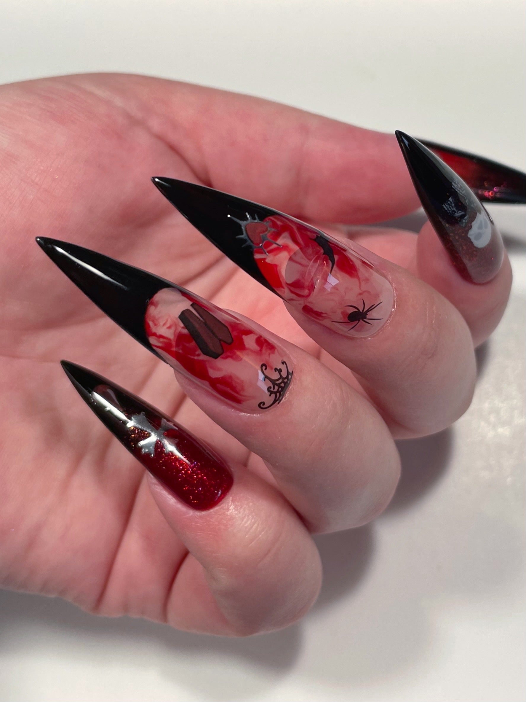 Close up of long stiletto nails with black French, red glitter, and stickers from the Vamp nail art sheet