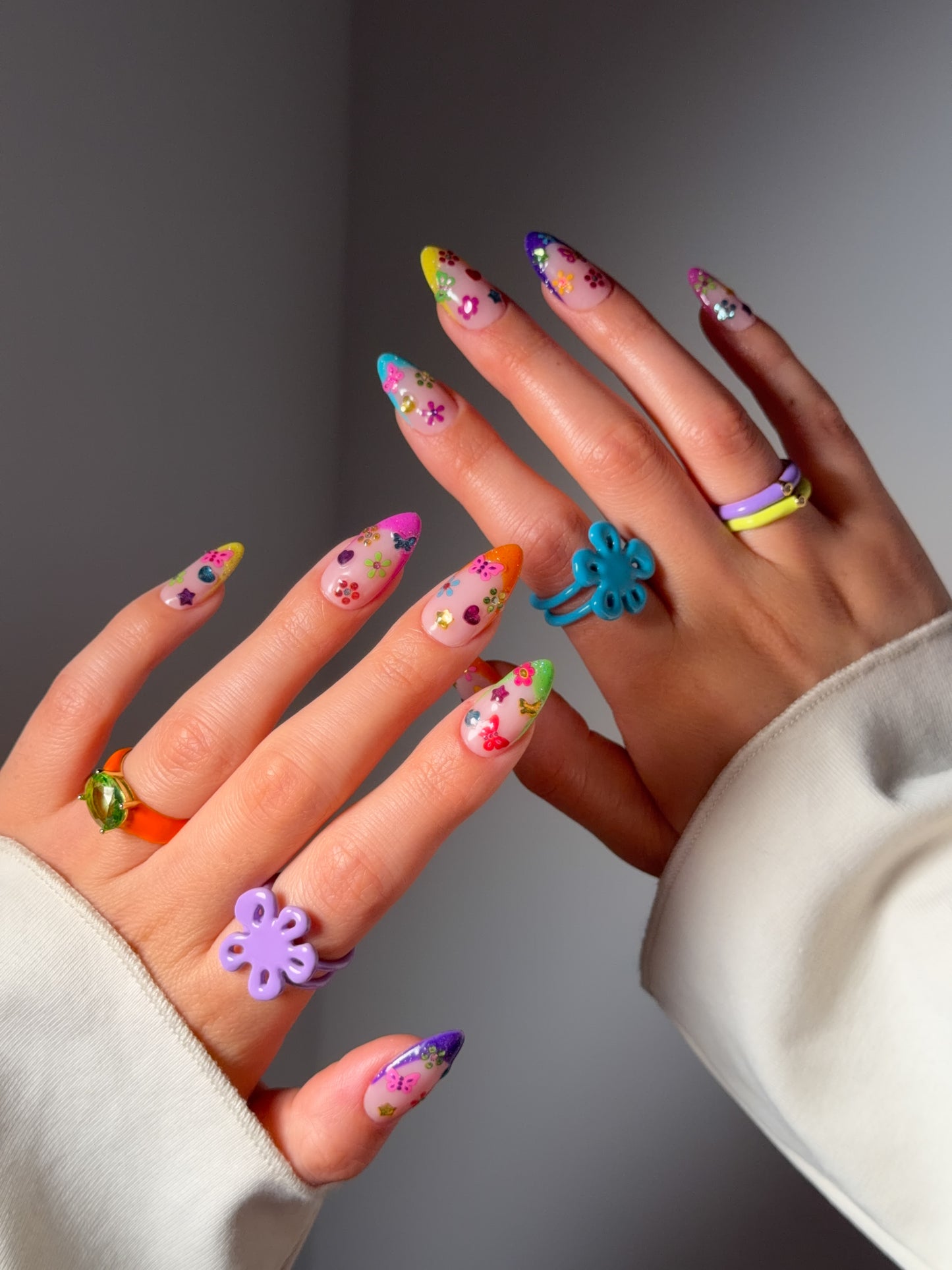 Hands with colorful nail art stickers and floral rings on a neutral background