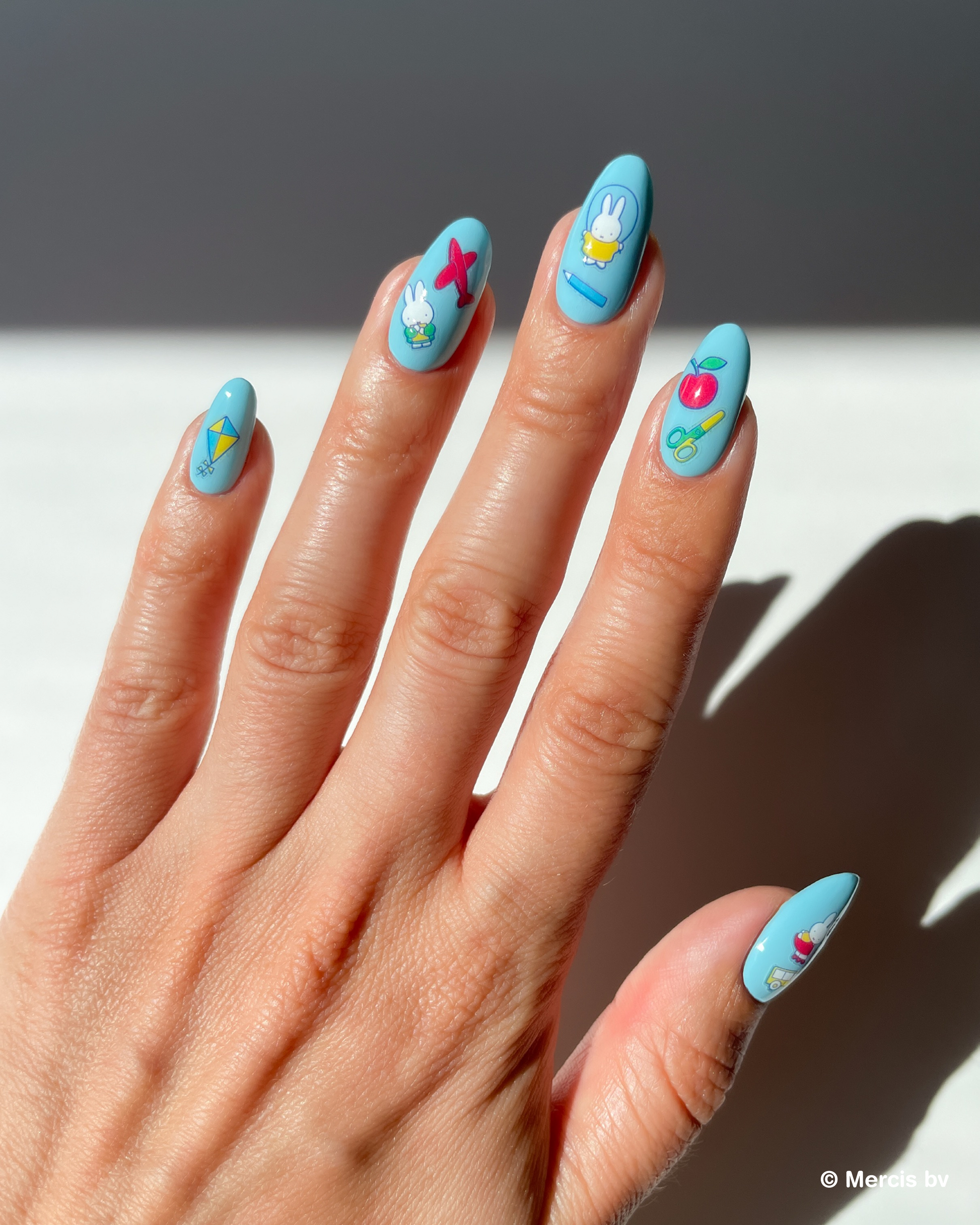 Hand with blue nail polish and miffy nail art stickers on a neutral background