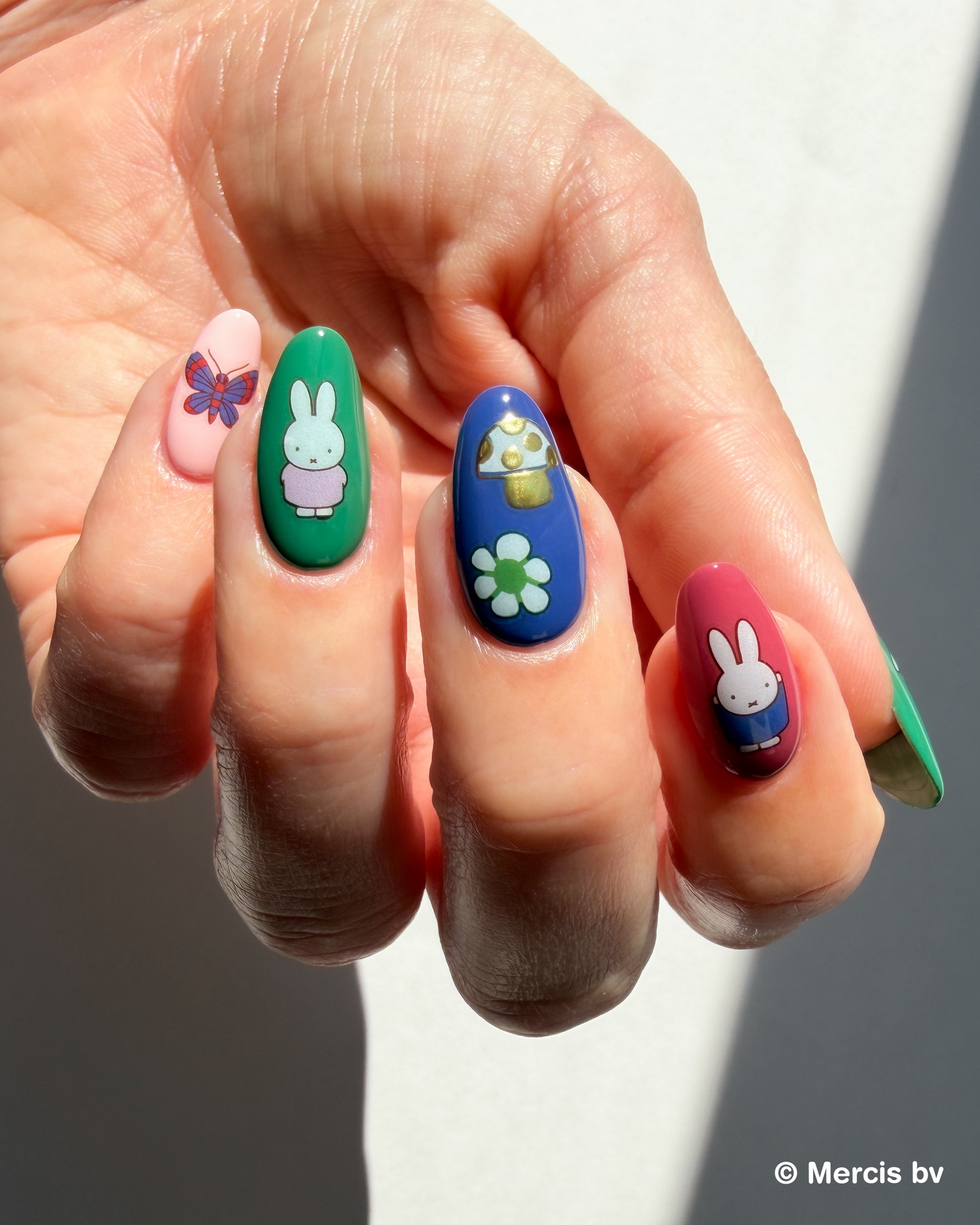 Hand with colorful nails and Miffy stickers on a neutral background