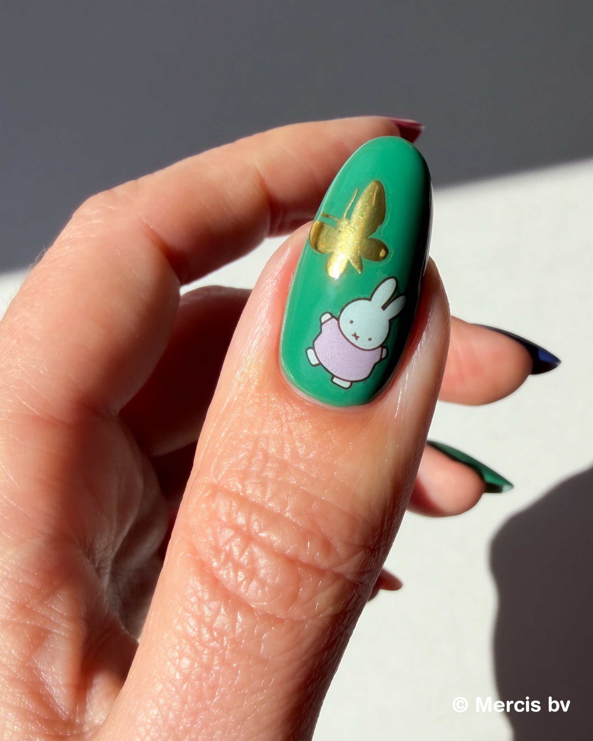 Nail with green polish with Miffy stickers on a neutral background.