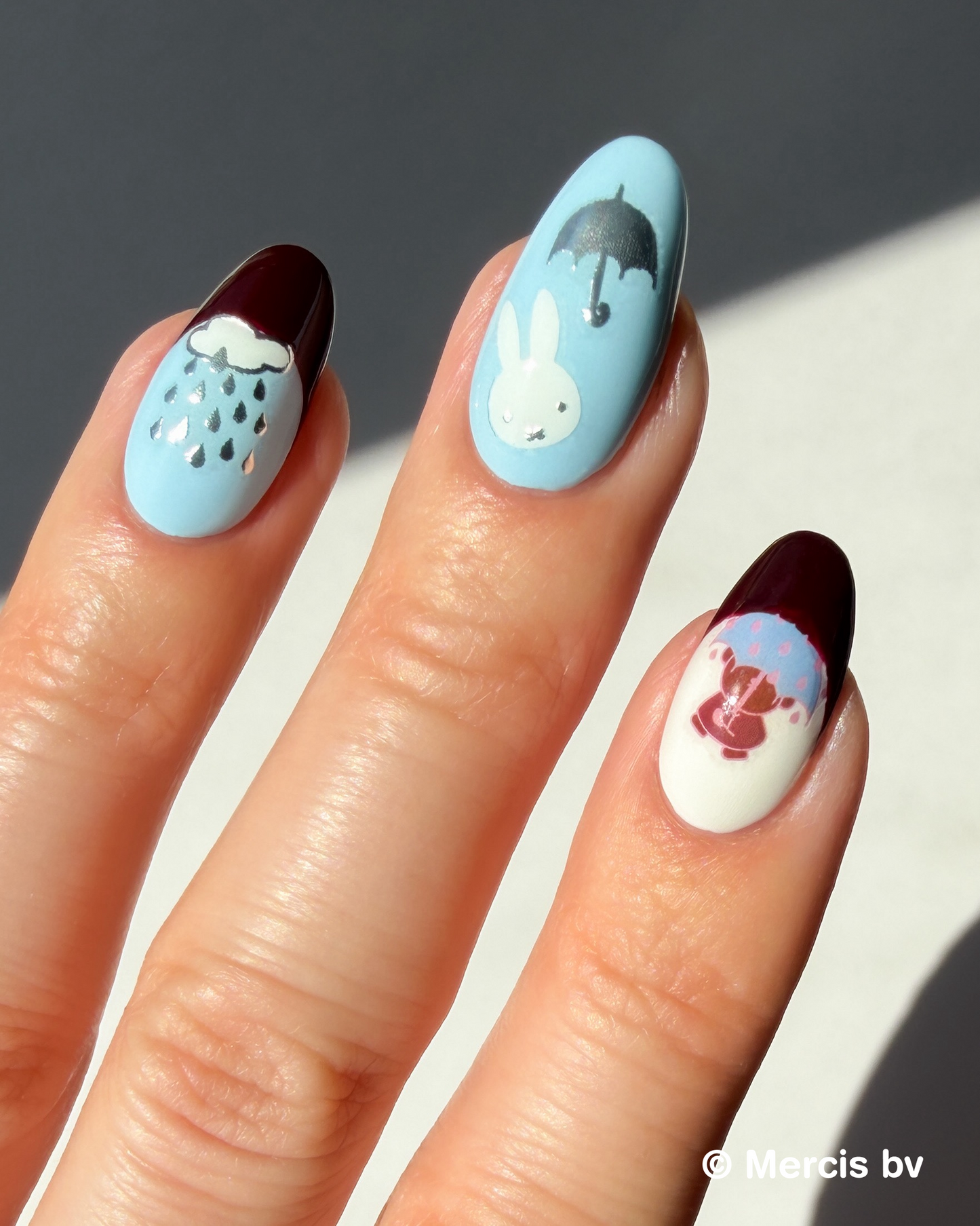 Hand with blue and dark red nails and Miffy stickers on a neutral background.