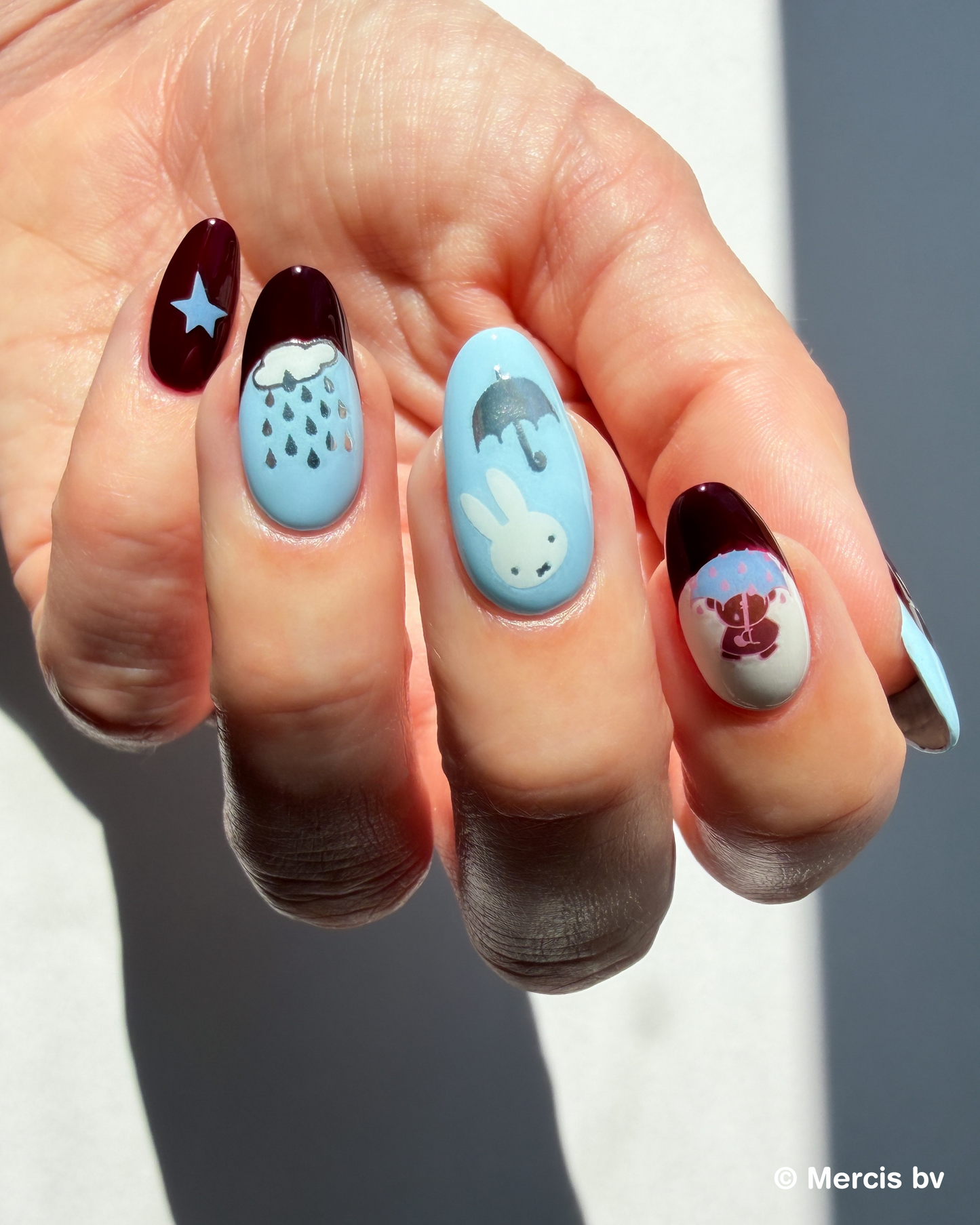 Hand with blue and dark red nails and Miffy stickers on a neutral background.