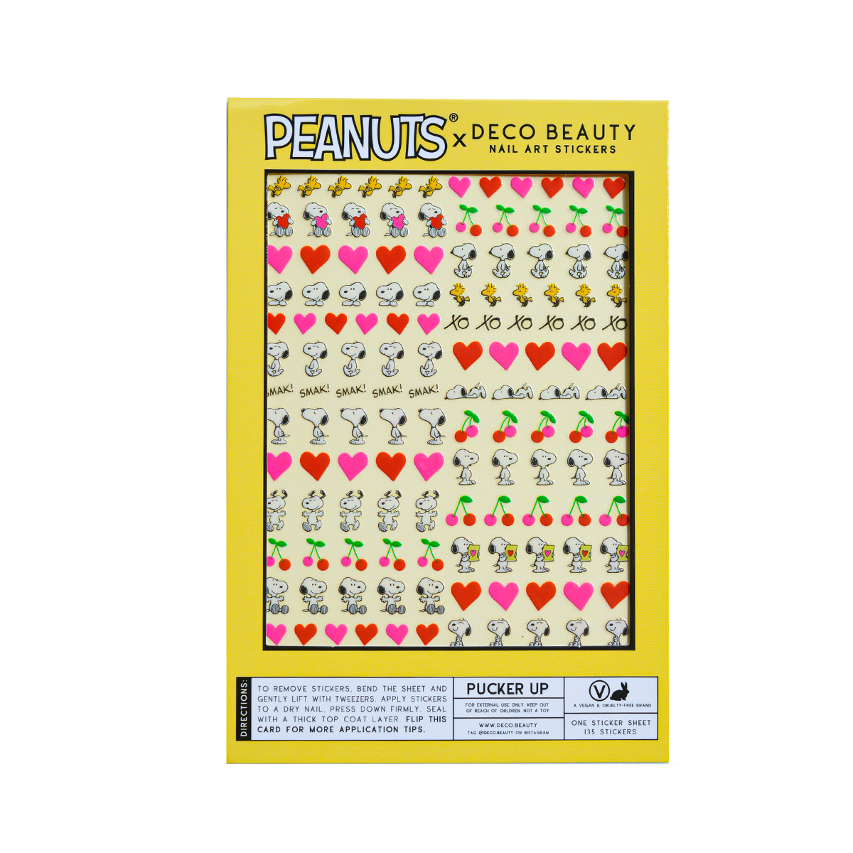 A flat lay of a sheet of Peanuts x Deco Beauty nail art stickers featuring Snoopy, Woodstock, hearts, cherries, and 'xo xo,' in yellow packaging.