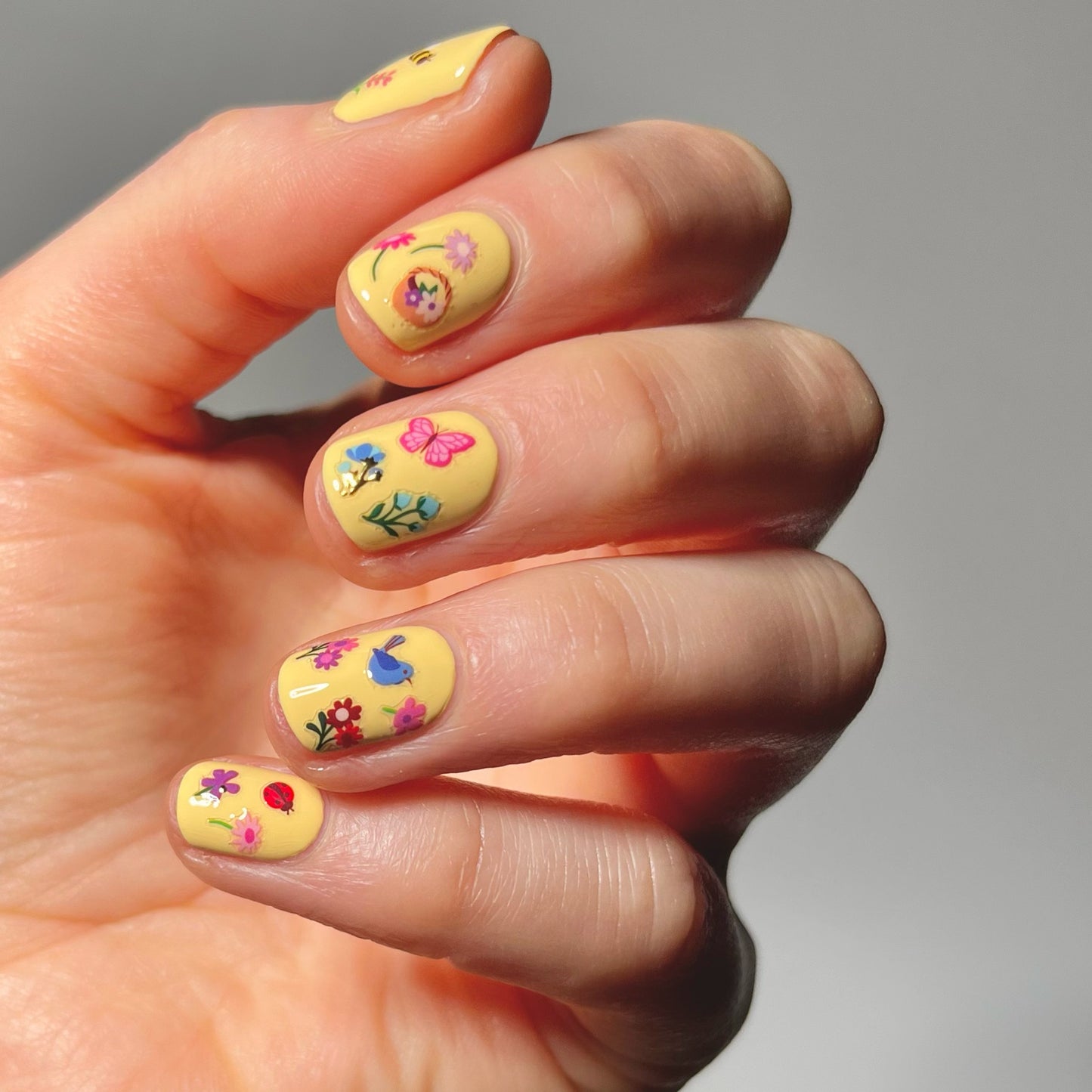 Hand with yellow nail polish and tiny flower stickers