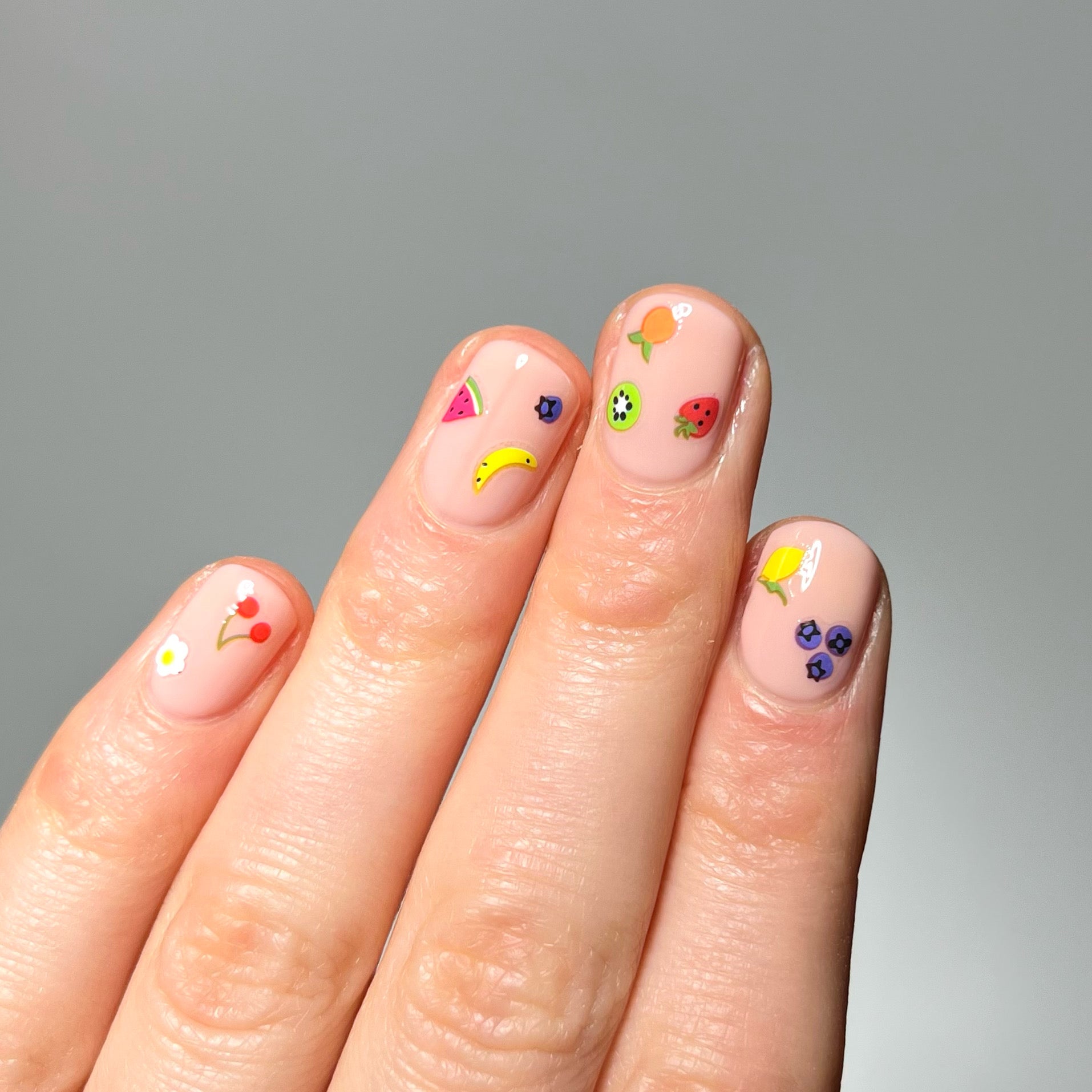 Hand with neutral nail polish and tiny fruit stickers