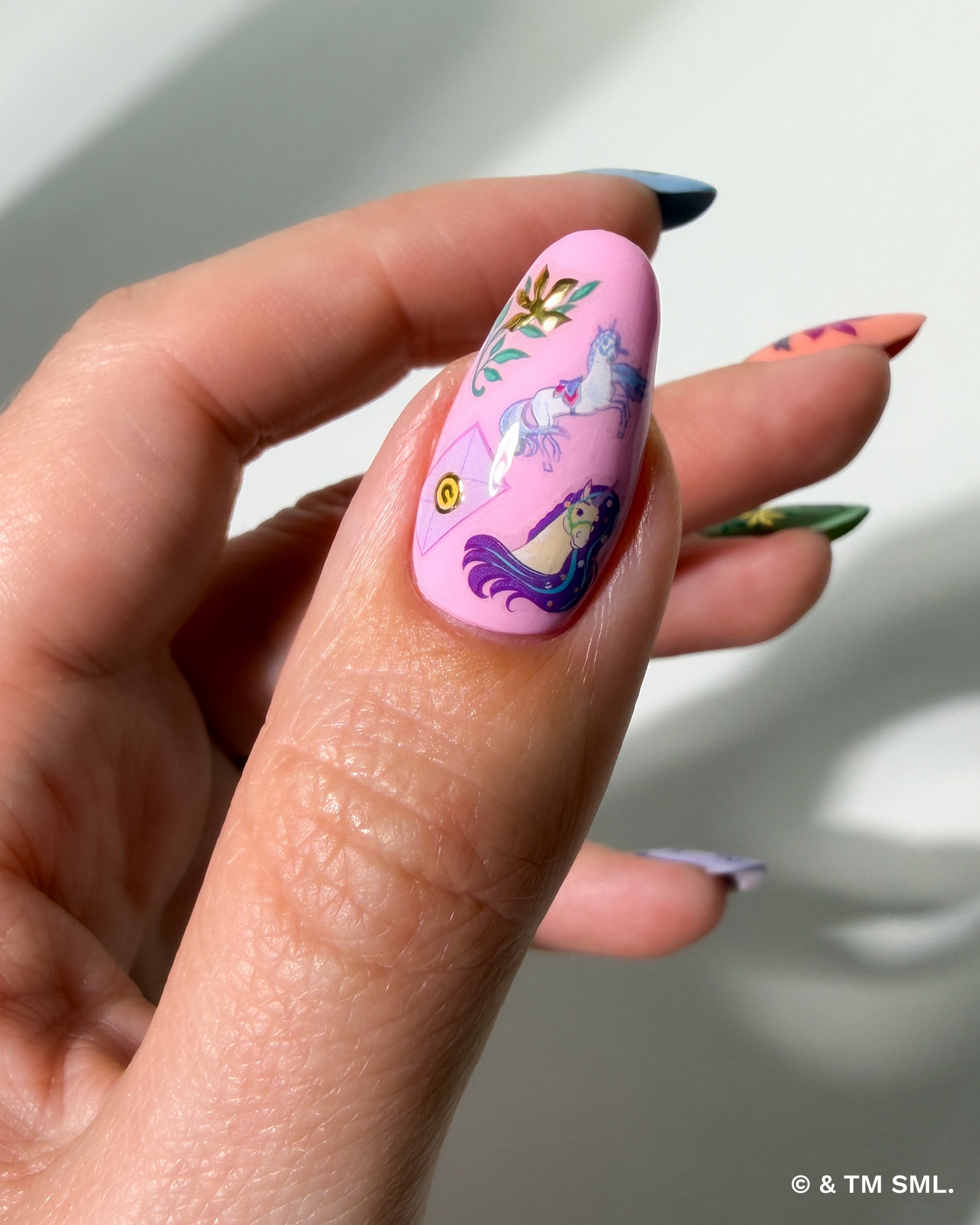 Hand with a pink nail featuring unicorn design against a neutral background