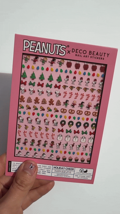 A gif of Peanuts x Deco Beauty Holiday Cheer nail art stickers, with festive stickers including Christmas trees, candy canes, snowmen, and Peanuts characters in light pink packaging.